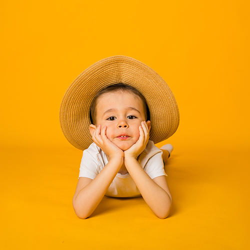 portrait-of-small-boy-in-white-t-shirt-and-straw-hat-looking-at-the-camera-on-yellow-surface-with-space-for-text